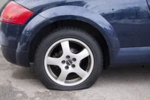 Blue car with puncture in tyre which is covered by car hire excess insurance